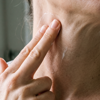 Fingers smoothing cream on the neck